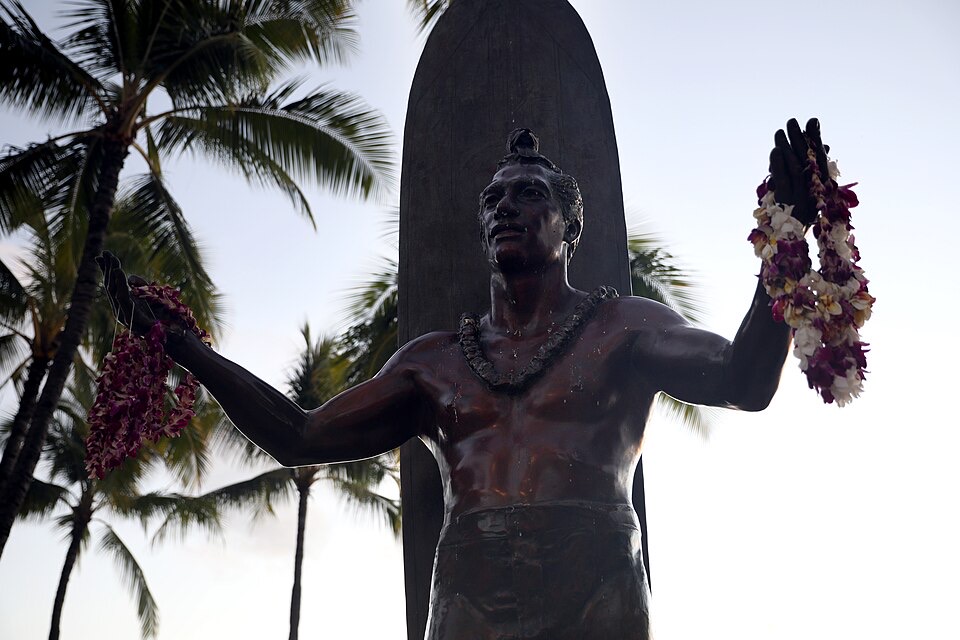 Bronze Duke Kahanamoku statue with leis draped on his outstretched arms at Kuhio Beach.
