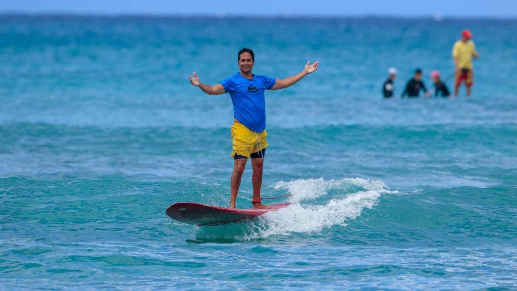 Beginner surf students riding small Waikiki waves with instructors alongside.